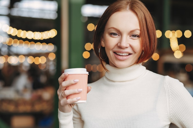 Optimistische mooie vrouw met geverfd haar, tevreden uitdrukking, draagt een coltrui