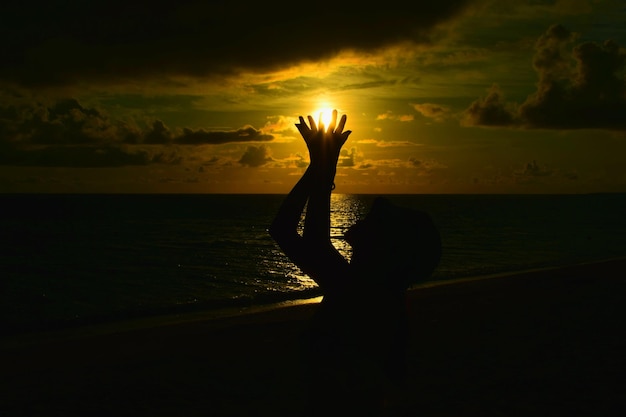 Foto optische illusie van een silhouet vrouw die de zon vasthoudt op het strand tegen de hemel tijdens de zonsondergang