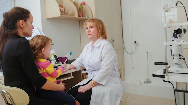 Photo optometrist checks child's eyesight - mother and child have consultation in ophthalmologist room, horizontal