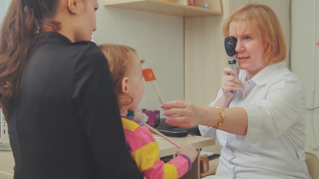 검안사는 아이의 시력을 확인합니다 - 안과 의사의 방에 있는 엄마와 아이, 수평