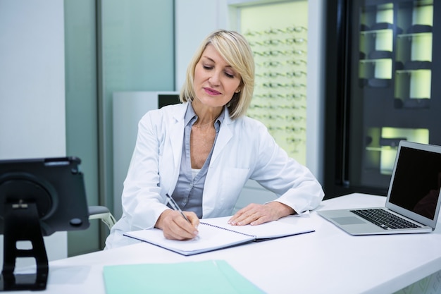 Foto optometrista scrivendo nel libro presso la clinica oculistica