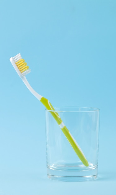 Oral hygiene. green toothbrush in a glass on a gentle blue.