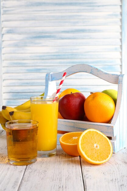 Orange and apple juice and fresh fruits in wooden box on wooden table on wooden wall background