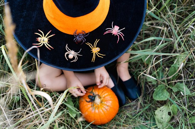 Orange autumn pumpkin in children's hands with spiders, decor for the Halloween holiday.