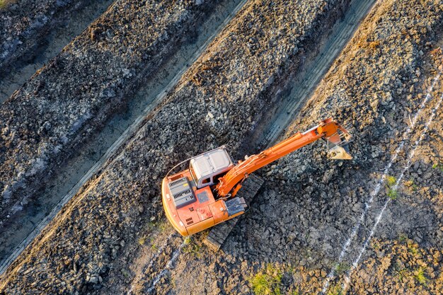 Orange bachkhoe is digging soil creating  grooves for planting parm and coconut in Thailand 