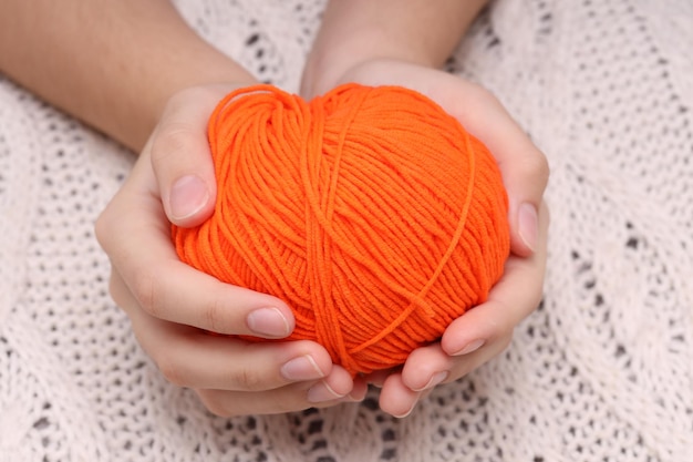 Orange ball of wool in hands on the background of a white knitted tablecloth High quality photo