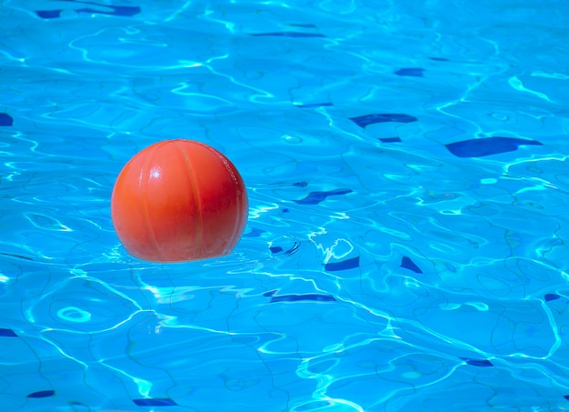 Photo orange beach ball floating in blue swimming pool, with place for your text.