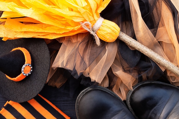 Orange and black Halloween flatlay. Witch clothes: stockings, boots, hat, broom, skirt