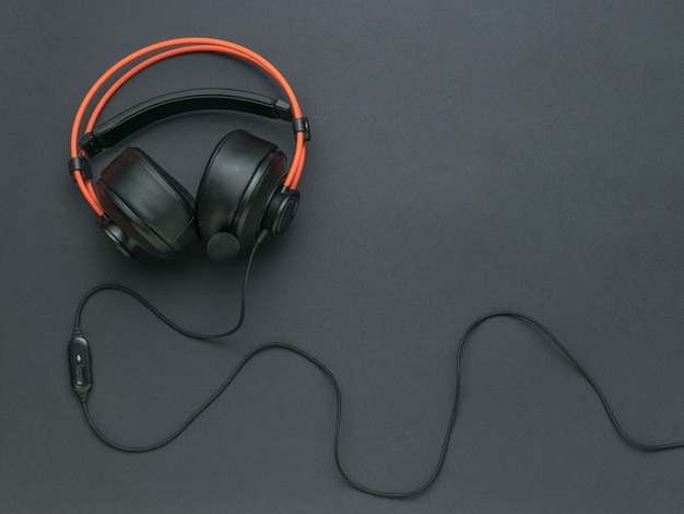 Orange and black headphones with a wire on a black background An accessory for listening to audio recordings