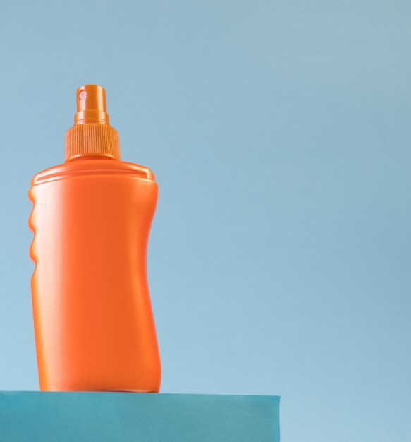 Orange bottle of sunscreen on the podium on a light blue background