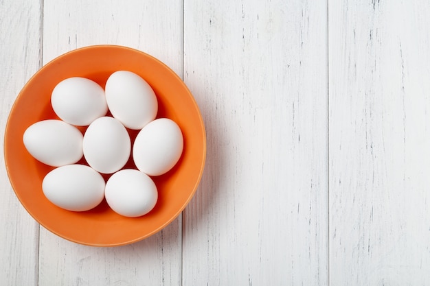 Orange bowl with white eggs on wooden table with copy space