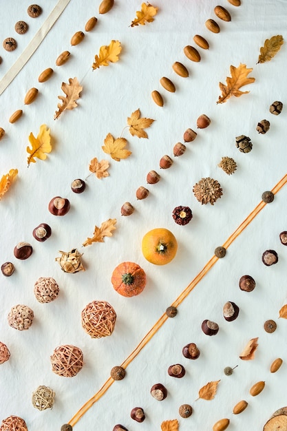 Orange, brown white Fall background. Top view on white textile. Abstract geometric diagonal pattern with pumpkins, acorns, nuts, Autumn leaves and wattle balls.