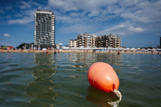 Orange buoy floating in the sea with a residential building in the background