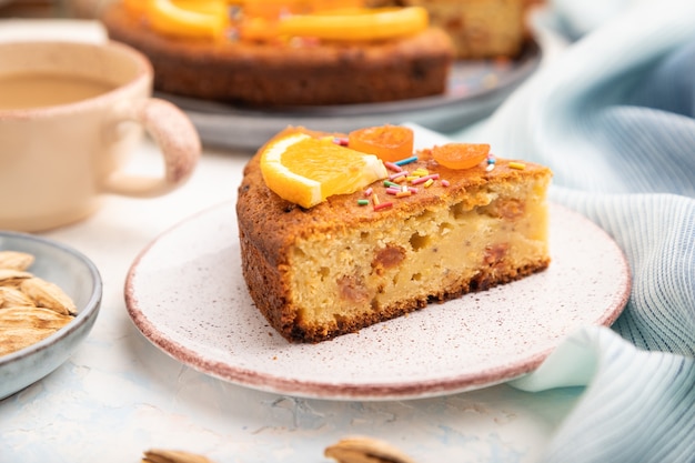 Orange cake with almonds and a cup of coffee on a white concrete background and blue linen textile.