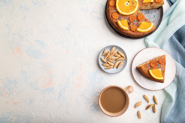 Orange cake with almonds and a cup of coffee on a white concrete table and blue linen textile. Top view, flat lay, copy space.