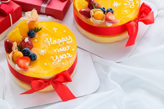 Orange cake with happy new year and topped with orange, strawberry, blueberry and Cape Gooseberry on white cloth , copy space and dessert concept