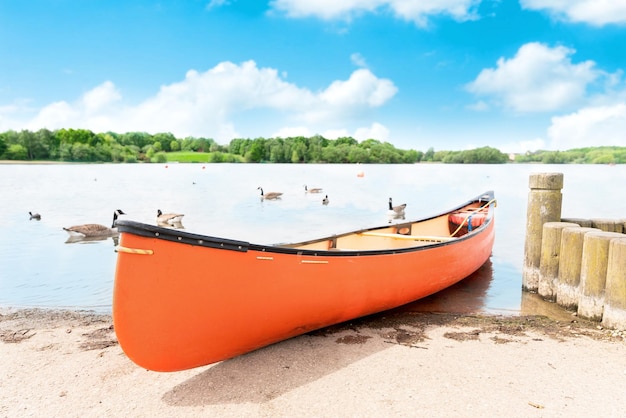 A orange canoe resting on a lakeshore in the public park on summer days