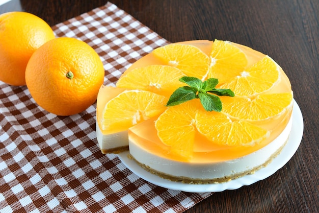 orange cheesecake with cut slice and mint on the brown tablecloth