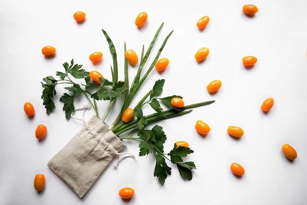 Orange cherry tomatoes flat lay with parsley greens in a cloth bag on a white background