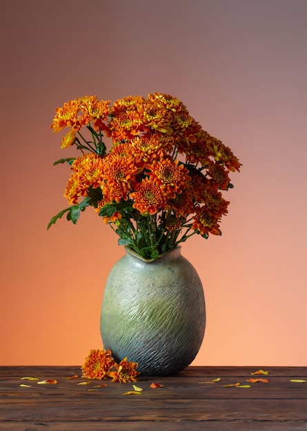 Orange chrysanthemums in vase on wooden background