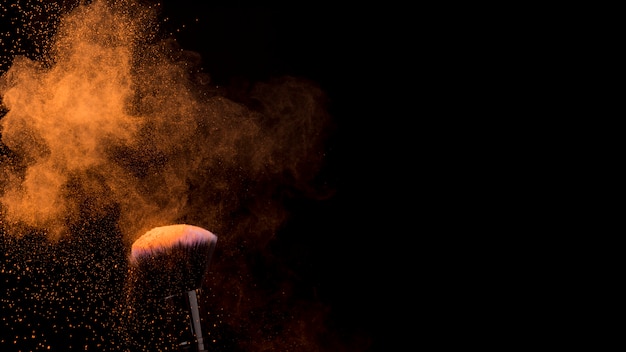 Photo orange cloud of powder and makeup brush on dark background