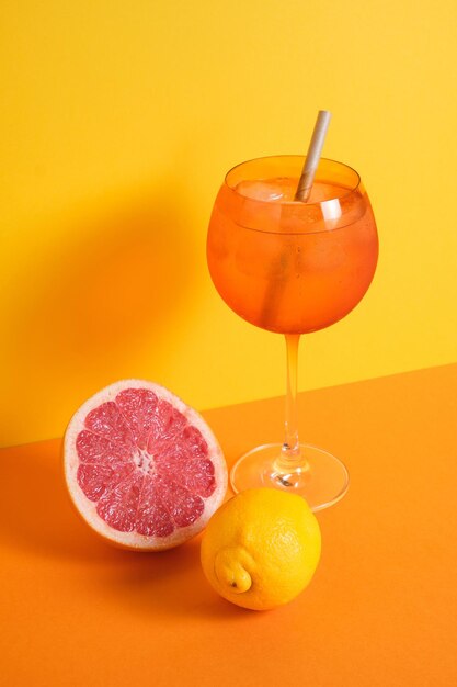 Orange cocktail glass with ice and straw accompanied with lemon and grapefruit on orange and yellow minimalistic background