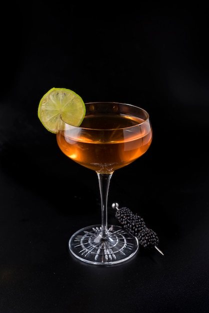 Orange cocktail with lemon slice and blackberry brochette on black background