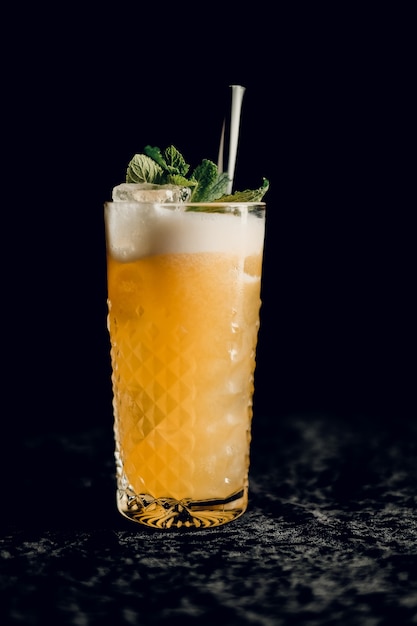 orange cocktail with mint in a beautiful glass with ice on a dark surface