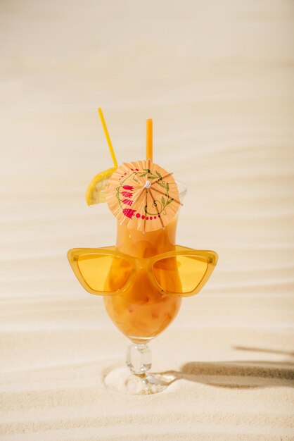 Orange cocktail with sunglasses and cocktail umbrella on sandy beach