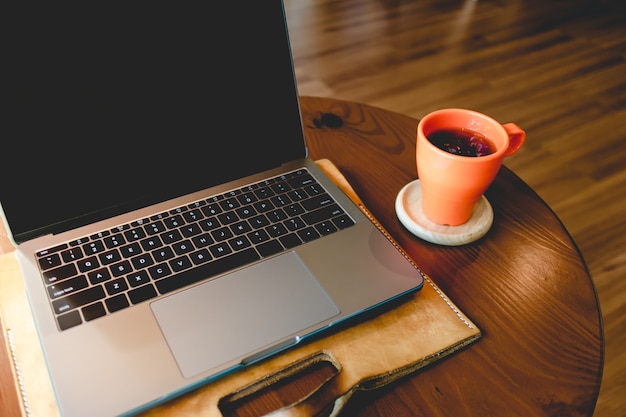 Orange coffee cup and laptop on the table in the cafe.