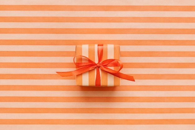 Orange color gift box on striped wrapping paper.