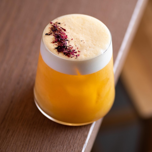 Orange colored cocktail with white foam on brown table