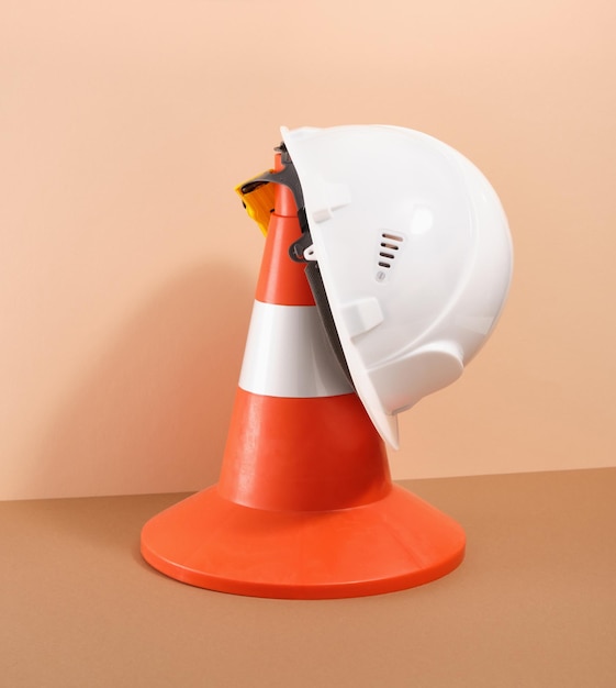 Photo orange construction cone and white head protection helmet on a beige background