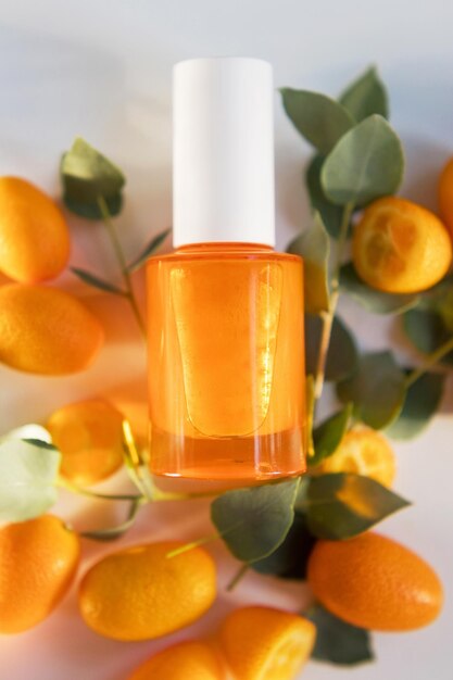 Foto bottiglia di vetro cosmetico arancione con gocce d'acqua, frutti di kumquat e foglie di eucalipto verde