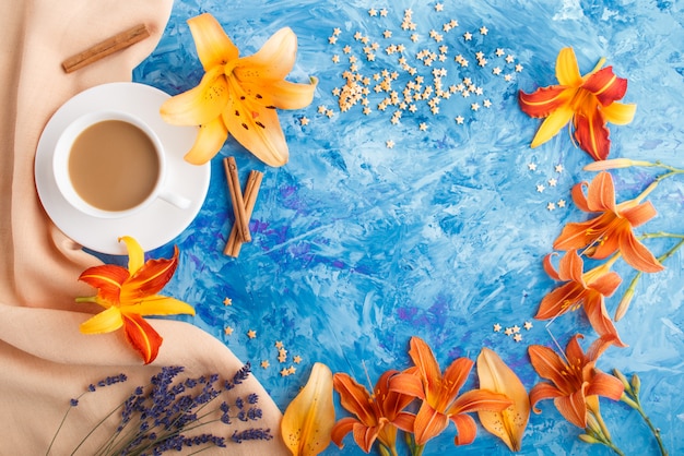 オレンジ色のデイリリーとラベンダーの花と青いコンクリート背景にコーヒーカップ