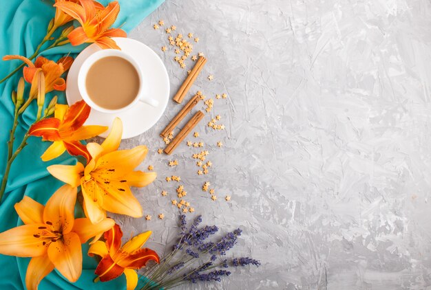 오렌지 하루 백합 및 라벤더 꽃과 파란색 섬유와 회색 구체적인 배경에 커피 한 잔. 평면도.