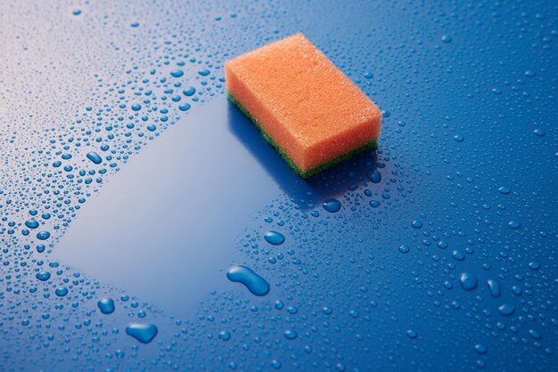 An orange double sided cleaning sponge paled on blue background covered with drops with copyspace