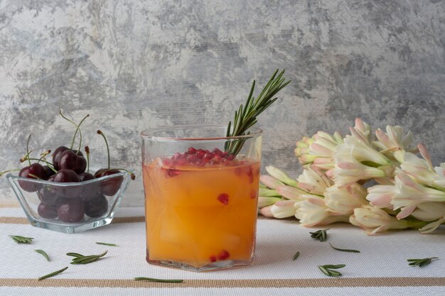 orange drink with red pomegranate and a branch of rosemary on a table accompanied by cherries