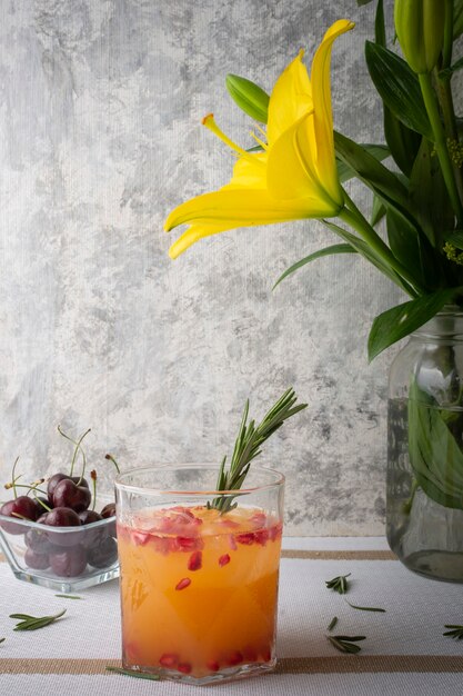 orange drink with red pomegranate and a branch of rosemary on a table accompanied by cherries