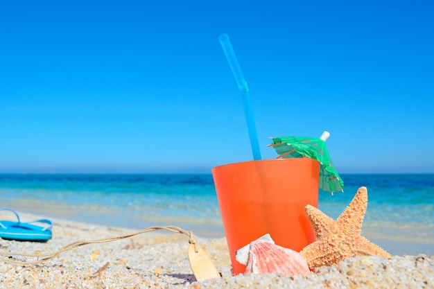 Orange drink with shell and umbrella by a tropical beach