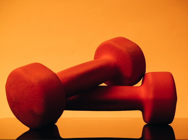 Orange dumbbells for fitness on an orange background. Reflected from the glass surface of the balance. concept of sports and healthy lifestyle.