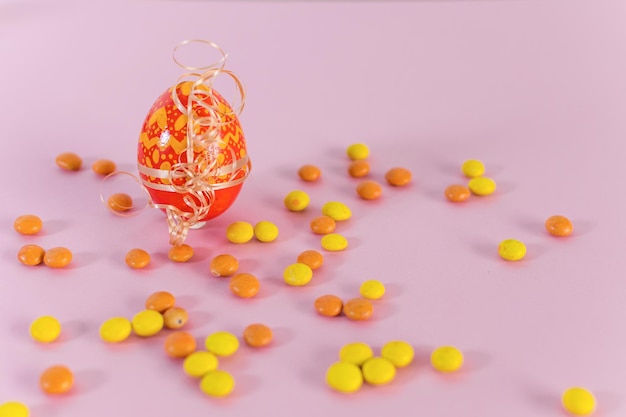 Orange Easter egg and candies on a pink background