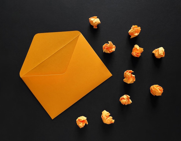 Orange envelope and crumpled orange paper balls on black\
background.