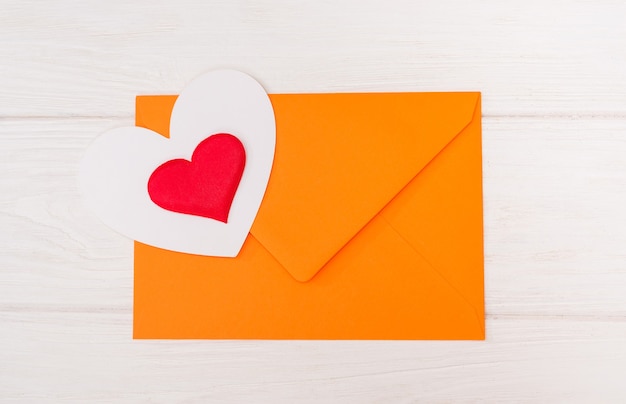 Orange envelope and two hearts on a white wooden background. View from above.