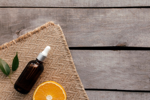 Orange essential oil in glass bottle with green leaf. Cosmetic concept on wooden background on sackcloth, isolated flat lay. 