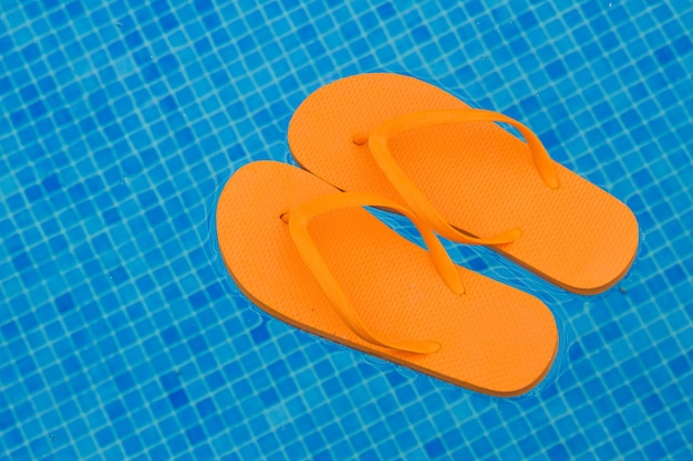 Orange flip flops floating in blue pool water