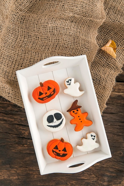 Orange gingerbread in pumpkin shape and ghosts Halloween sweets lie in a wooden tray Tasty cookie on table Top view