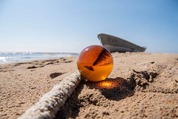 写真 海の近くの砂の上のオレンジ色のガラス玉