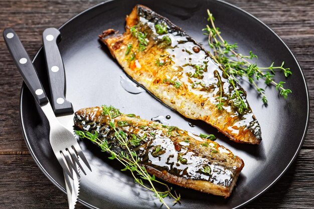 Orange glazed fried mackerel fillets with spices and thyme on a black plate