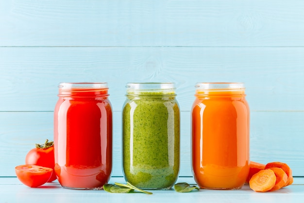 Photo orange/green/red colored smoothies / juice in a jar on a blue.